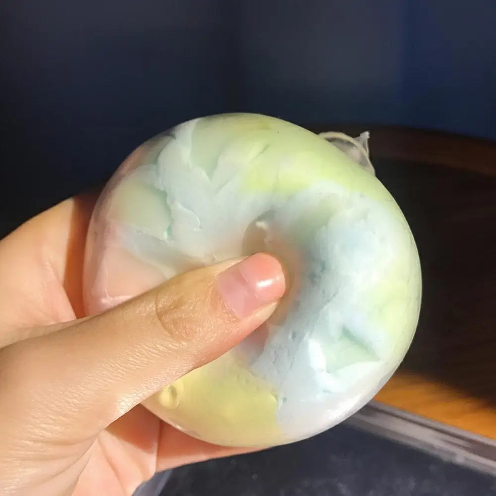 Thumb pressing into a rainbow wax crack squishy ball, showing the crackled pastel wax shell