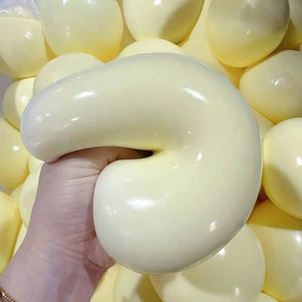 Pale yellow gooey stress ball being squeezed and stretched in a hand over a pile of yellow balls