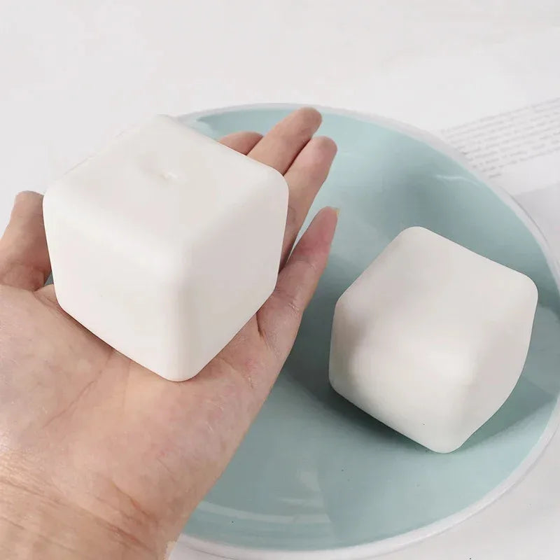 Two white tofu cube squishies, one held in an open hand, on a pale blue plate
