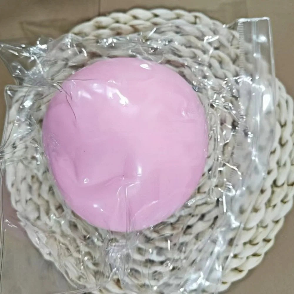 Pink gooey stress ball, about 10 cm, in a clear bag on a woven mat