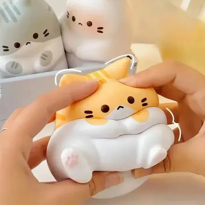 Orange and white cat squishy being squeezed in two hands, with other cat squishy styles behind it; style is random, 1 per order