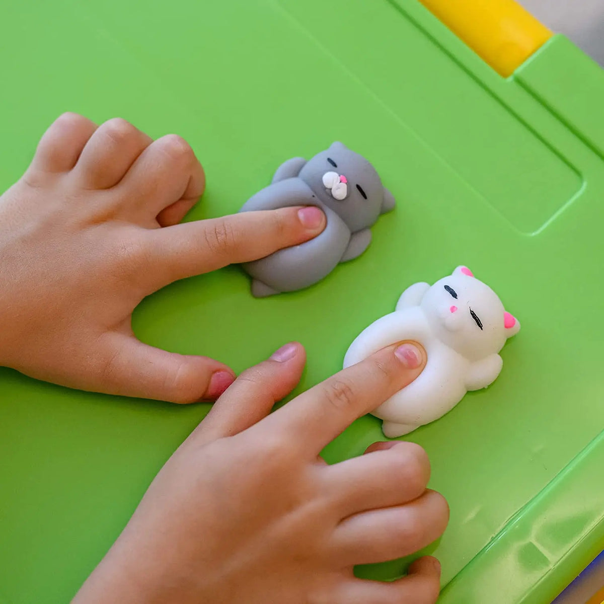 Child's fingers pressing gray and white mini mochi cat squishies on a green desk
