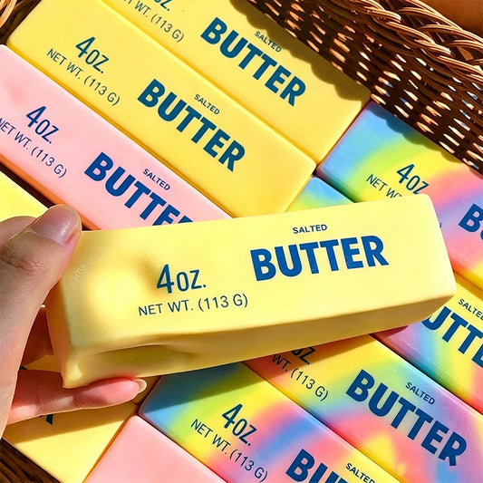 Hand holding a yellow butter stick squishy printed with "4 oz. Salted Butter" wrapper text, other butter squishies behind it