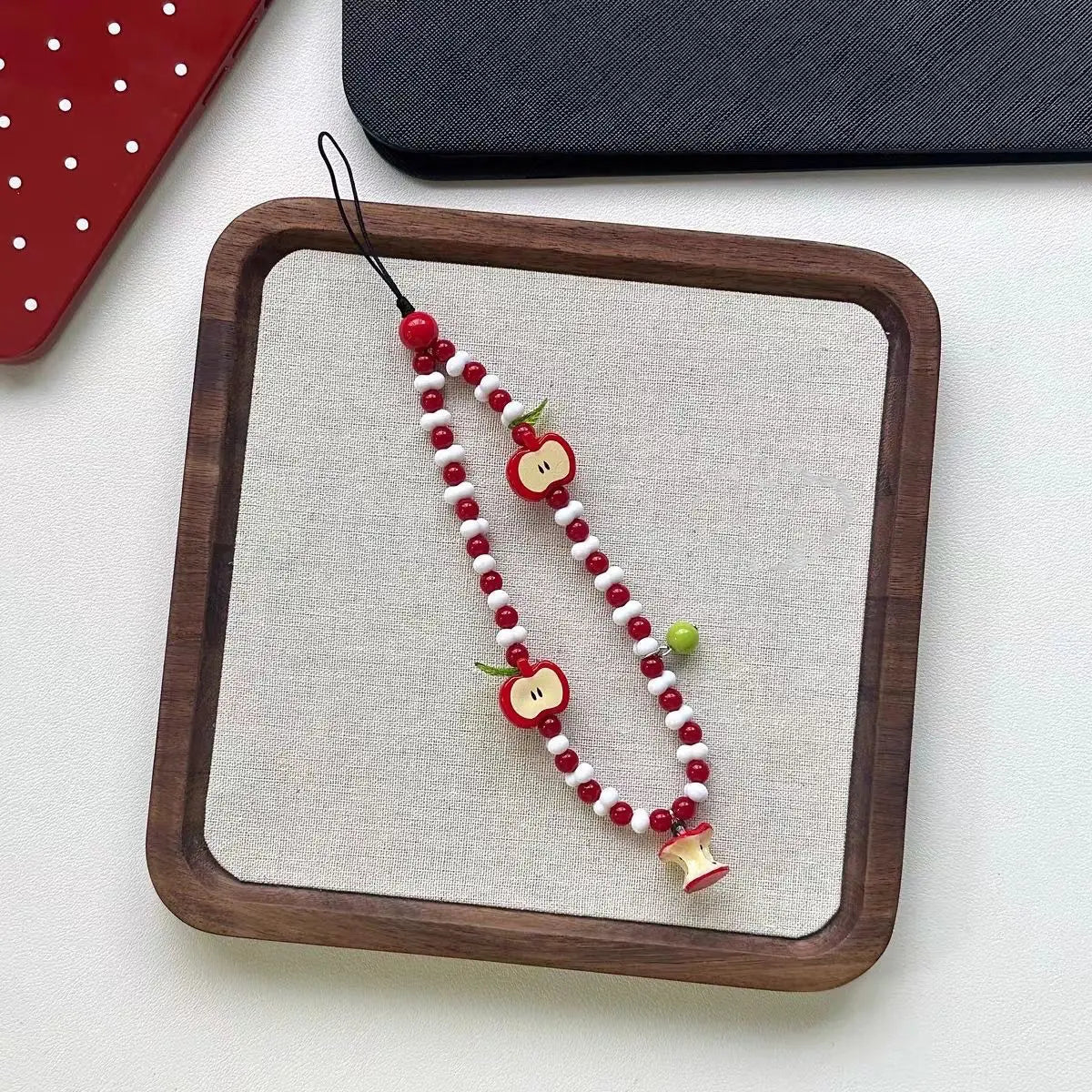 Apple beaded charm strap laid flat on a linen tray
