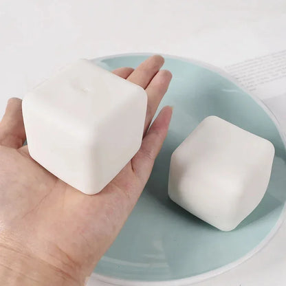 Two white tofu cube squishies, one held in an open hand, on a pale blue plate