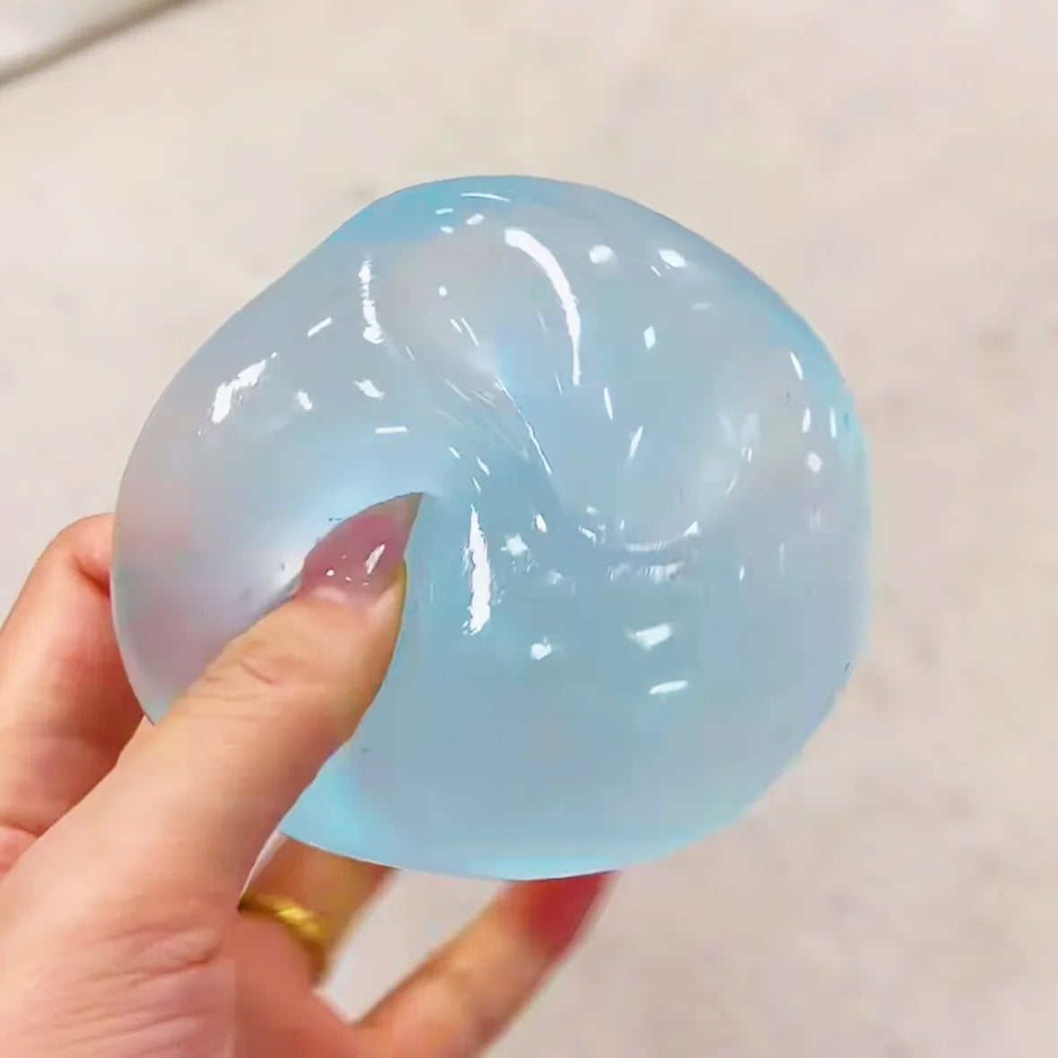 Blue jelly squeeze ball being squeezed with a thumb