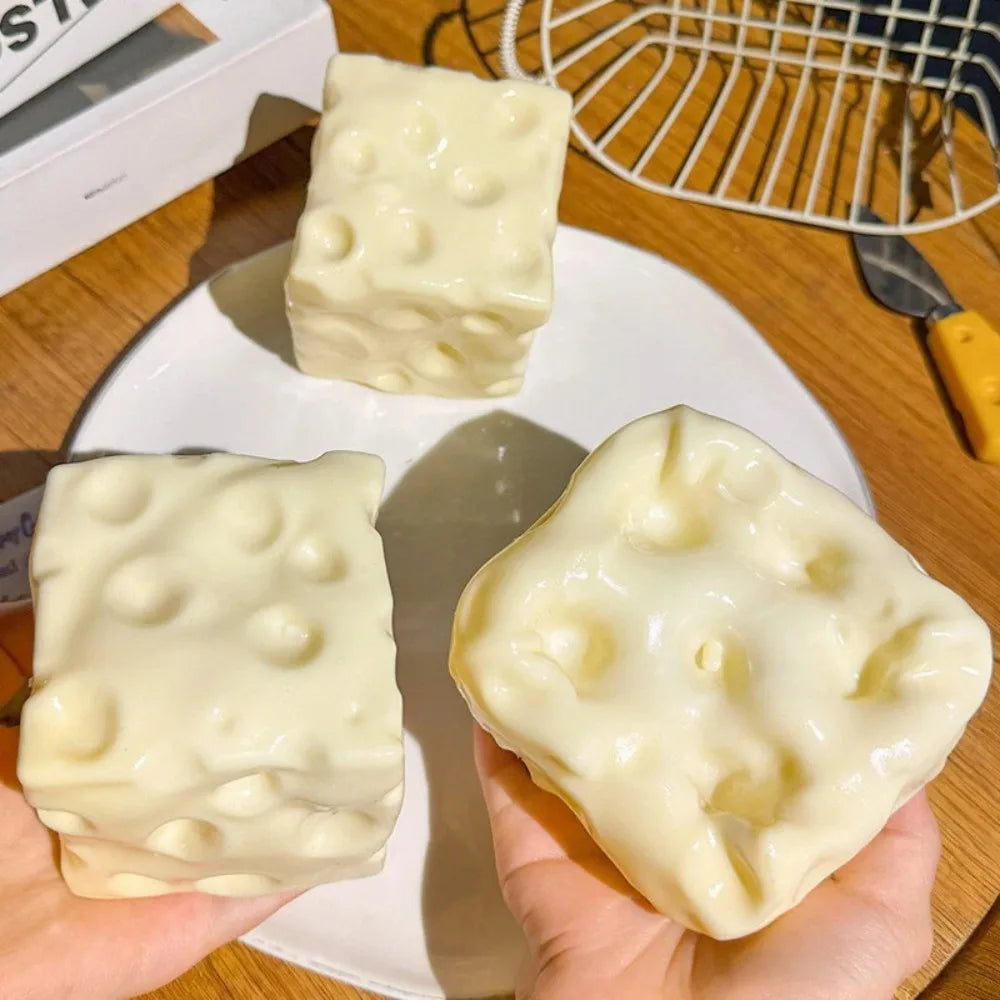 Cheese block squishies with holes on a plate, one squeezed flat in a hand