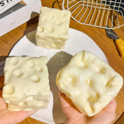 Cheese block squishies with holes on a plate, one squeezed flat in a hand
