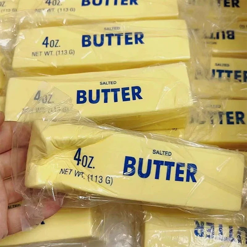 Yellow butter stick squishy being squeezed in hand above a pile of butter stick squishies
