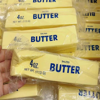 Yellow butter stick squishy being squeezed in hand above a pile of butter stick squishies