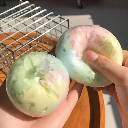 Two pastel rainbow wax crack squishy balls held in hands, one pressed to show the cracked wax shell