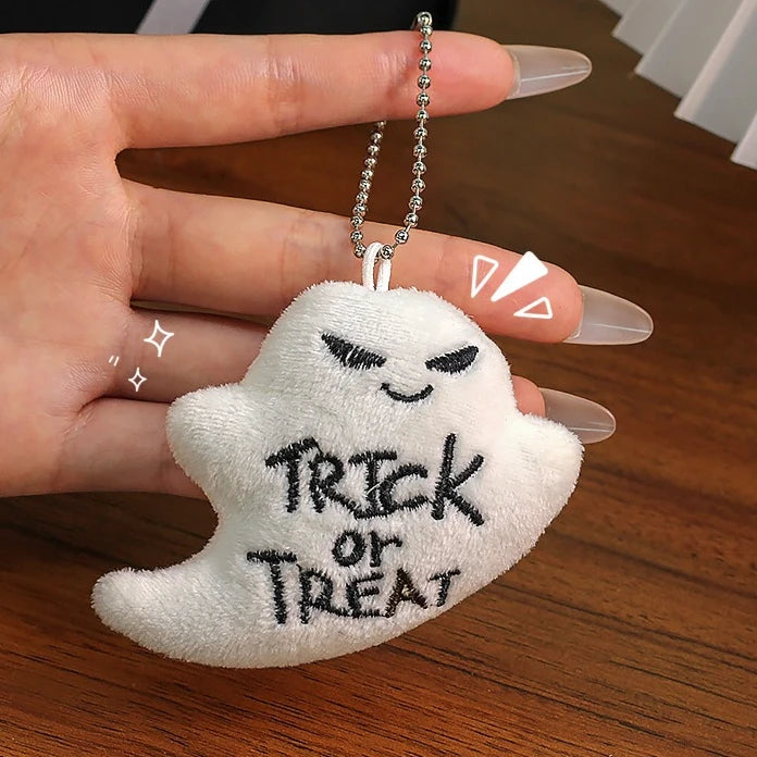 White plush ghost keychain with "Trick or Treat" embroidery on a ball chain, held in a hand