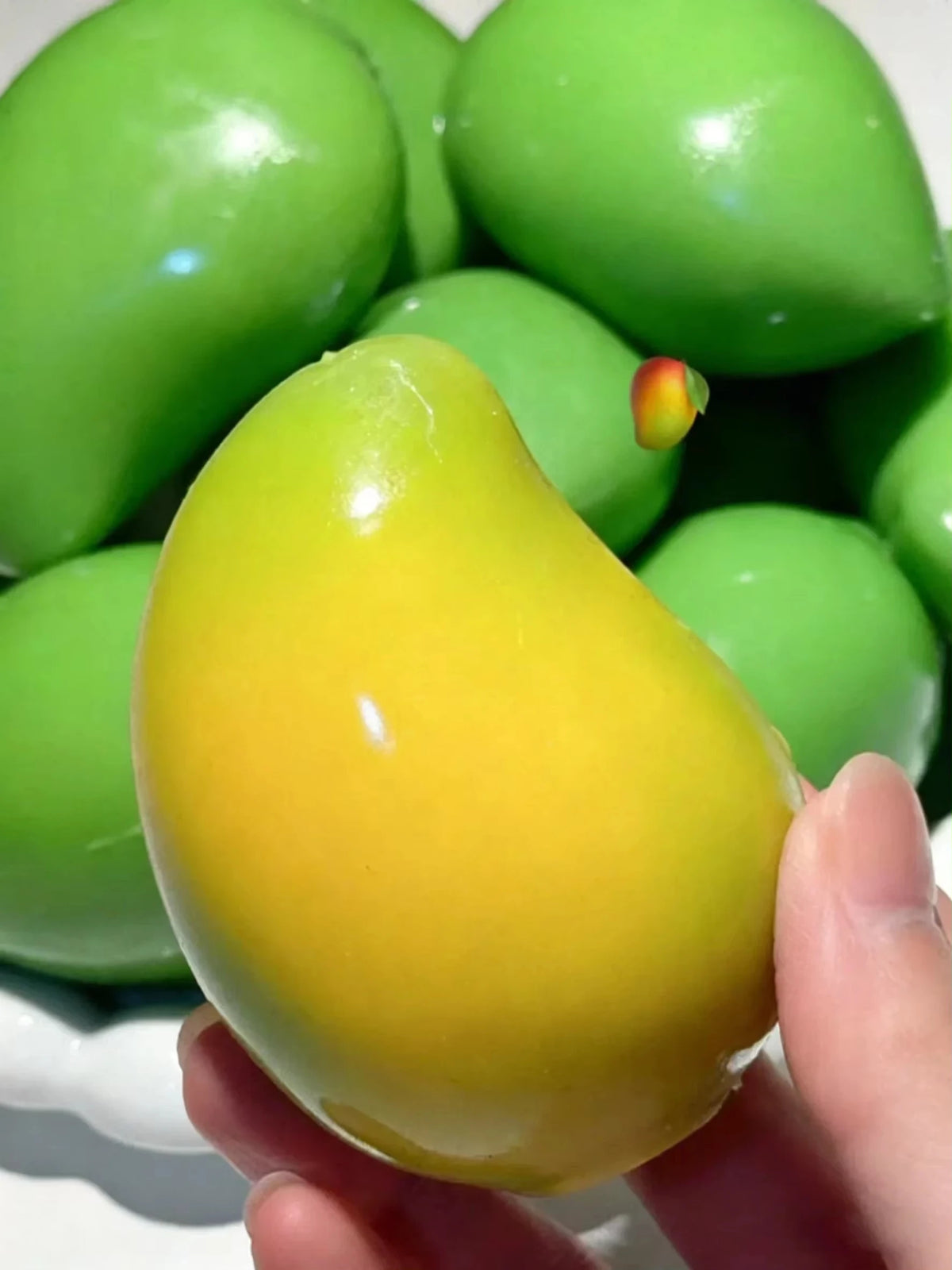 Yellow-green mango squishy held in front of a pile of green mango squishies (colors vary)