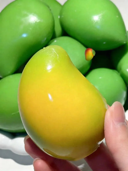 Yellow-green mango squishy held in front of a pile of green mango squishies (colors vary)